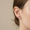 Close-up of an ear wearing a colorful earring against a neutral background